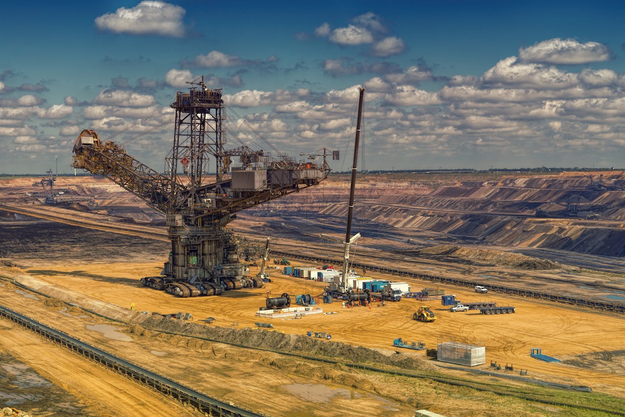 about-01 Aerial view of heavy machinery operating in a vast open-pit mine under a cloudy sky.
